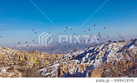 Pigeons are flying at Pigeon Valley in Cappadocia. Birds flying together with snowy volcanic landscape in Cappadocia, Turkey 68942859