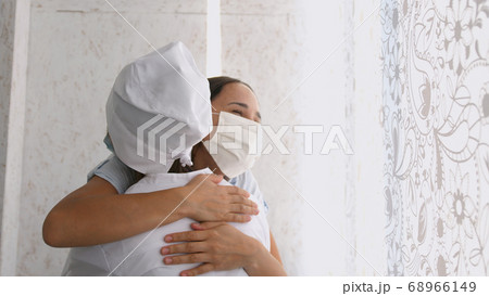 Smiling young female patient in mask with female doctor in white uniform thanking for help or feeling excited about healthcare treatment results at meeting. 68966149