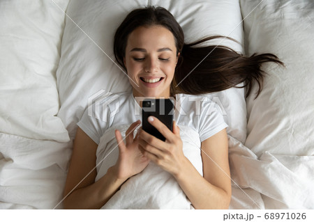 Top view smiling young woman using phone, relaxing in bed 68971026