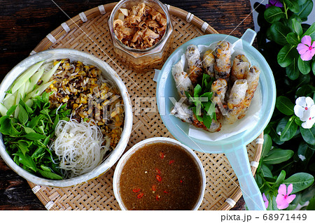 tray of Vietnamese vegan food for lunch time, bowl of noodles with deep fried corn spring rolls and sliced cucumber, basil leaf, dipping sauce tray of Vietnamese vegan food for lunch time, bowl of noodles with deep fried corn spring rolls and sliced cucumber, basil leaf, dipping sauce 68971449