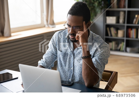 Thoughtful doubtful African American businessman looking at laptop screen Thoughtful doubtful African American businessman looking at laptop screen 68973506