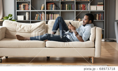 Smiling African American man relaxing on couch with phone 68973718