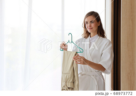 young cheerful caucasian woman in white pajama choosing clothes in wardrobe in bedroom 68973772