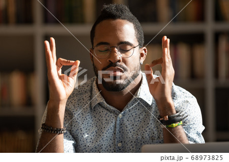 Close up mindful African American man wearing glasses meditating 68973825