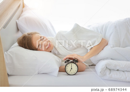 Upset young caucasian woman lying in bed, wake up late and overslept trying to stop alarm clock 68974344