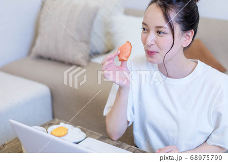 パソコンを見ながらおやつを食べる若い女性 68975790