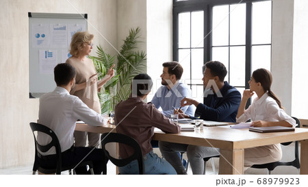 Serious mature old female company leader explaining marketing sales strategy. Serious mature old female company leader explaining marketing sales strategy. 68979923