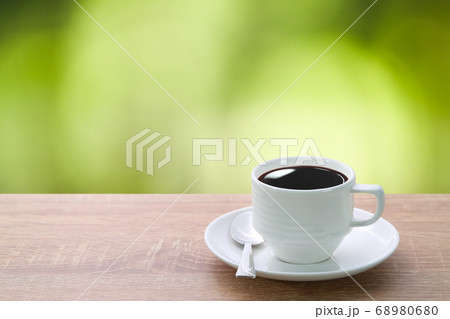 a cup of coffee and spoon on wood desk with beautiful green nature background 68980680