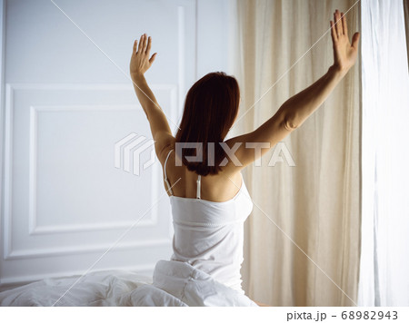 Woman stretching in bed after waking up, back view, entering a day happy and relaxed after good night sleep. Good morning and new day for brunette. Concept of Weekend, holidays Woman stretching in bed after waking up, back view, entering a day happy and relaxed after good night sleep. Good morning and new day for brunette. Concept of Weekend, holidays 68982943