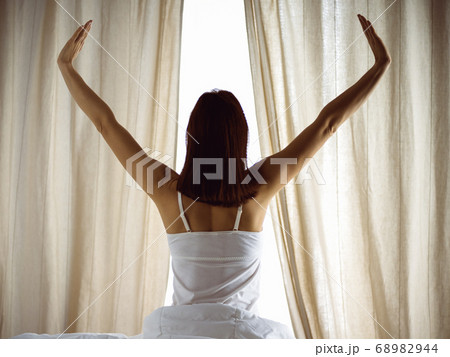 Woman stretching in bed after waking up, back view, entering a day happy and relaxed after good night sleep. Good morning and new day for brunette. Concept of Weekend, holidays Woman stretching in bed after waking up, back view, entering a day happy and relaxed after good night sleep. Good morning and new day for brunette. Concept of Weekend, holidays 68982944