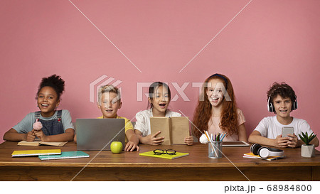 Remote schooling. Group of boys and girls with learning materials and devices sitting at desk over pink background 68984800