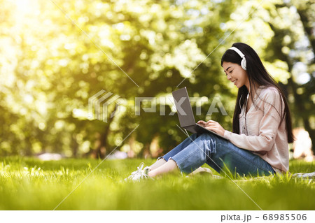 Joyful Asian Student Girl Preparing For Exam With Laptop Outdoors, Wearing Headphones Joyful Asian Student Girl Preparing For Exam With Laptop Outdoors, Wearing Headphones 68985506