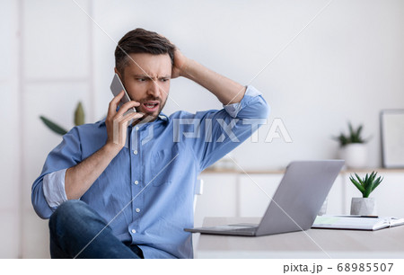 Frustrated businessman having problems with computer, talking on cellphone with customer support Frustrated businessman having problems with computer, talking on cellphone with customer support 68985507