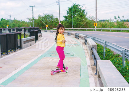 Little child girl to ride scooter in outdoor sports ground on sunny summer day Little child girl to ride scooter in outdoor sports ground on sunny summer day 68993283