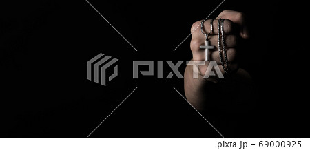 Crucifix pendant or cross sign made from silver and hold in man hand. represent praying for someone that pass away from World pandemic coronavirus and close-up shot black background Crucifix pendant or cross sign made from silver and hold in man hand. represent praying for someone that pass away from World pandemic coronavirus and close-up shot black background 69000925