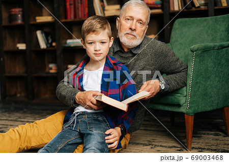 Portrait of child boy sitting with his grandfather and reading an interesting book Portrait of child boy sitting with his grandfather and reading an interesting book 69003468