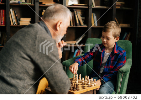 Back view of pensive grandfather playing chess with grandson, thinking about next step in chess game 69003702