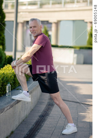 Mature grey-haired male stretching his knee outside 69005148