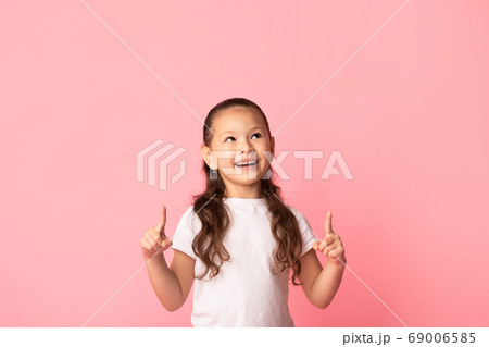 Happy asian girl pointing fingers up at copy space Happy asian girl pointing fingers up at copy space 69006585
