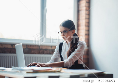 Cute brunette girl in eyeglasses typing and looking serious Cute brunette girl in eyeglasses typing and looking serious 69006653