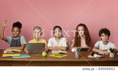 Focused black girl and her friends ready to answer lesson at desk over pink background, free space 69006902