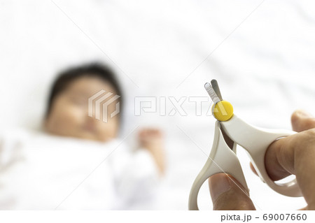 寝ている赤ちゃんと、赤ちゃん用爪切りを持った男性の手 寝ている赤ちゃんと、赤ちゃん用爪切りを持った男性の手 69007660