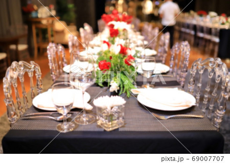 A blurred image of a dinner table with red roses. And green decorative leaves 69007707