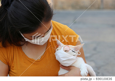 Masked Asian woman and her cat with eyeglasses prevent germs. Masked Asian woman and her cat with eyeglasses prevent germs. 69010836
