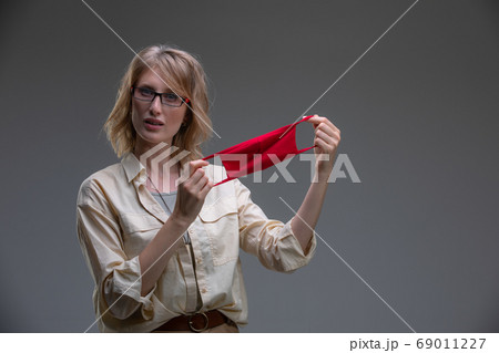 Blond young female in red protective mask against viruses, holds her head. 69011227