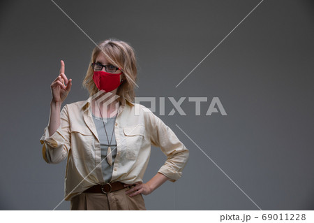 Blond young female in red protective mask against viruses, holds her head. 69011228