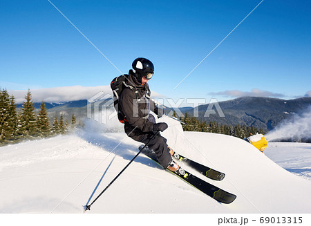 Man skiing on prepared slope with fresh snow. Snow gun machine making artificial snowfall. Magic nature on background. Man skiing on prepared slope with fresh snow. Snow gun machine making artificial snowfall. Magic nature on background. 69013315