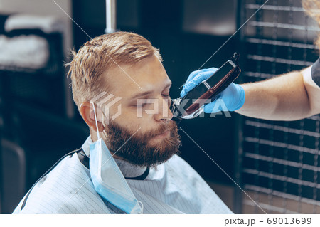Man getting hair cut at the barbershop wearing mask during coronavirus pandemic 69013699