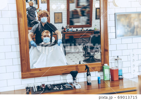 Man getting hair cut at the barbershop wearing mask during coronavirus pandemic 69013715