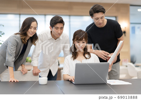 データを確認しながらパソコン操作する女性社員とその側でアドバイスと談笑をする男性上司達 データを確認しながらパソコン操作する女性社員とその側でアドバイスと談笑をする男性上司達 69013888