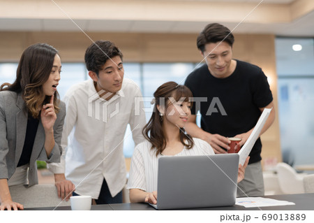 データを確認しながらパソコン操作する女性社員とその側でアドバイスと談笑をする男性上司達 データを確認しながらパソコン操作する女性社員とその側でアドバイスと談笑をする男性上司達 69013889