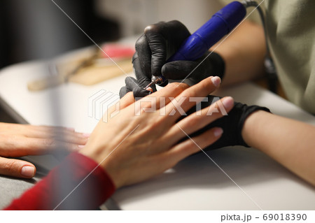 Professional in black gloves make mechanized manicure to visitor in studio. 69018390