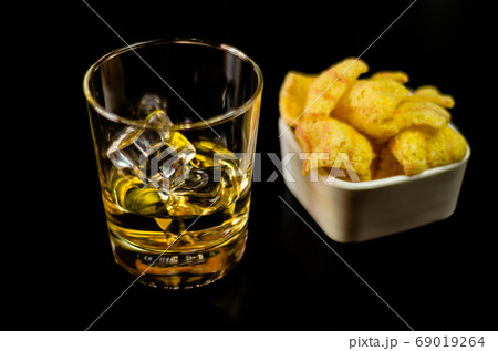 glass of whiskey with ice cubes and salty snacks 69019264