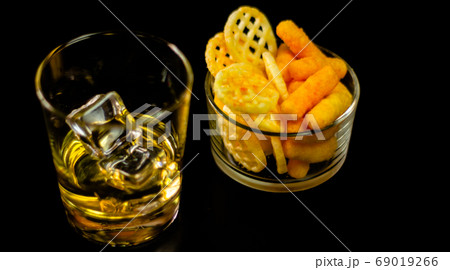 glass of whiskey with ice cubes and salty snacks 69019266