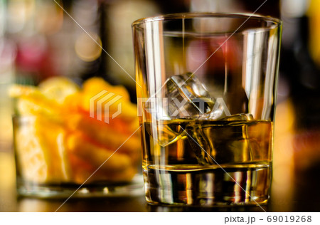 glass of whiskey with ice cubes and salty snacks 69019268