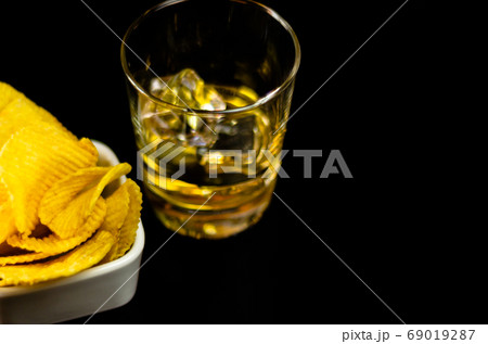 glass of whiskey with ice cubes and salty snacks 69019287