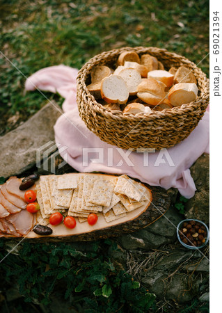 Wicker basket of bread on a bed on the ground with a wooden stand and biscuit biscuits, tomatoes and ham on it. Wicker basket of bread on a bed on the ground with a wooden stand and biscuit biscuits, tomatoes and ham on it. 69021394