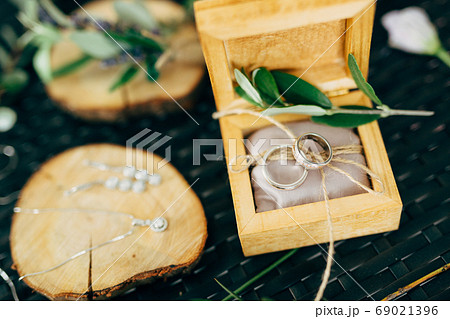 Open wooden box with wedding rings and a wooden stand with earrings and a chain with a pendant. Open wooden box with wedding rings and a wooden stand with earrings and a chain with a pendant. 69021396