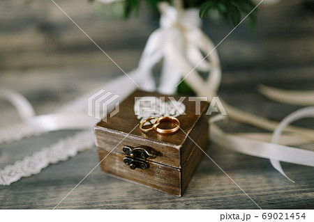 Closed wooden box with a heart and gold rings for the bride and groom on a background of white ribbons. 69021454