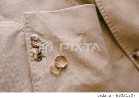 Two gold wedding rings on the sleeve of a beige men's jacket with buttons. 69021507