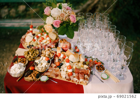 Festive table with flowers and clean empty champagne glasses with cheese and cold cuts on a wooden cutting board. 69021562