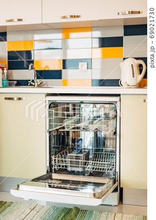 An open, empty dishwasher in a white kitchen decorated with blue, yellow and white tiles. 69021730