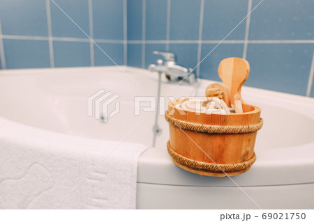 Wooden ladle with shower accessories on the rim of the corner bath near the terry towel. Wooden ladle with shower accessories on the rim of the corner bath near the terry towel. 69021750