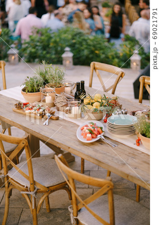 A festive table with fresh flowers in pots and lemons in a deep plate in a restaurant with chairs and guests on a blurred background. A festive table with fresh flowers in pots and lemons in a deep plate in a restaurant with chairs and guests on a blurred background. 69021791