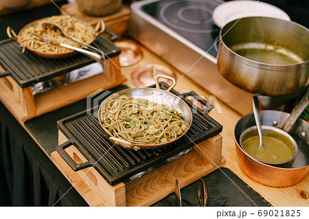Frying pans with spaghetti on a cast iron stove in the kitchen. Frying pans with spaghetti on a cast iron stove in the kitchen. 69021825