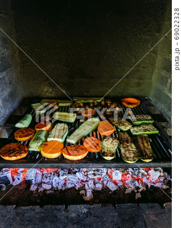 Grilled vegetables. Courgette, mushrooms and pumpkin on a metal grill over red coals. 69022328